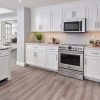 Millennium Off White kitchen cabinets with a stainless range, tile backsplash and light wood floor