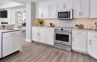 Millennium Off White kitchen cabinets with a stainless range, tile backsplash and light wood floor